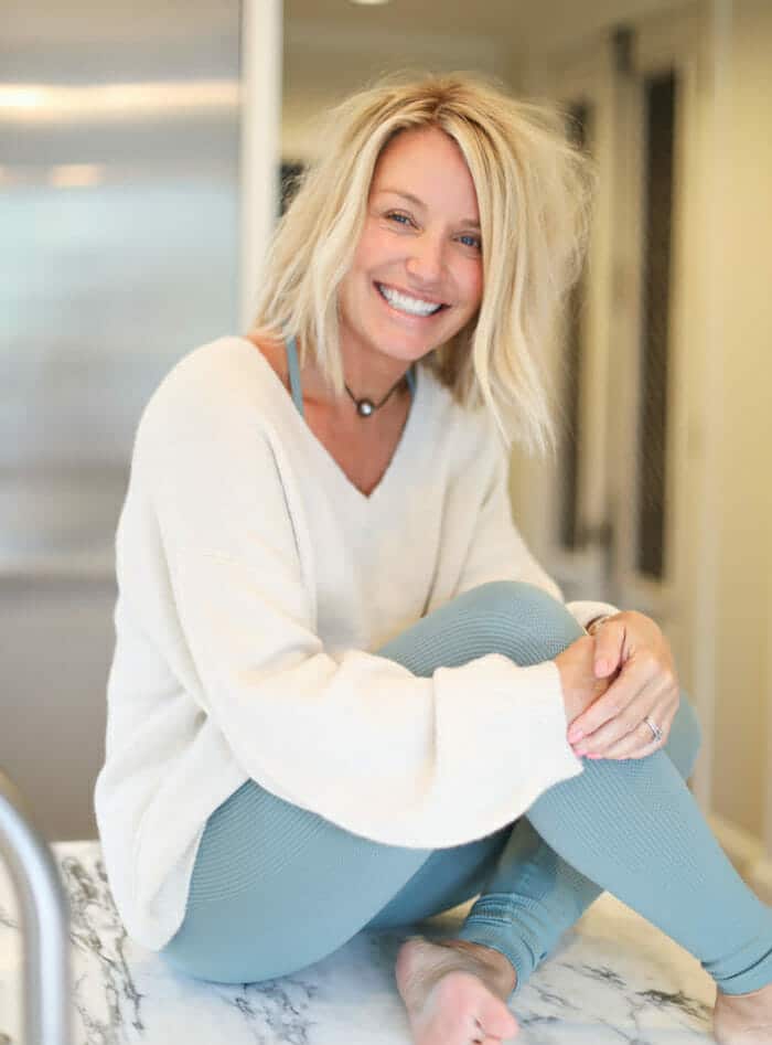 Menopause health coach Deanna smiling sitting on a kitchen counter